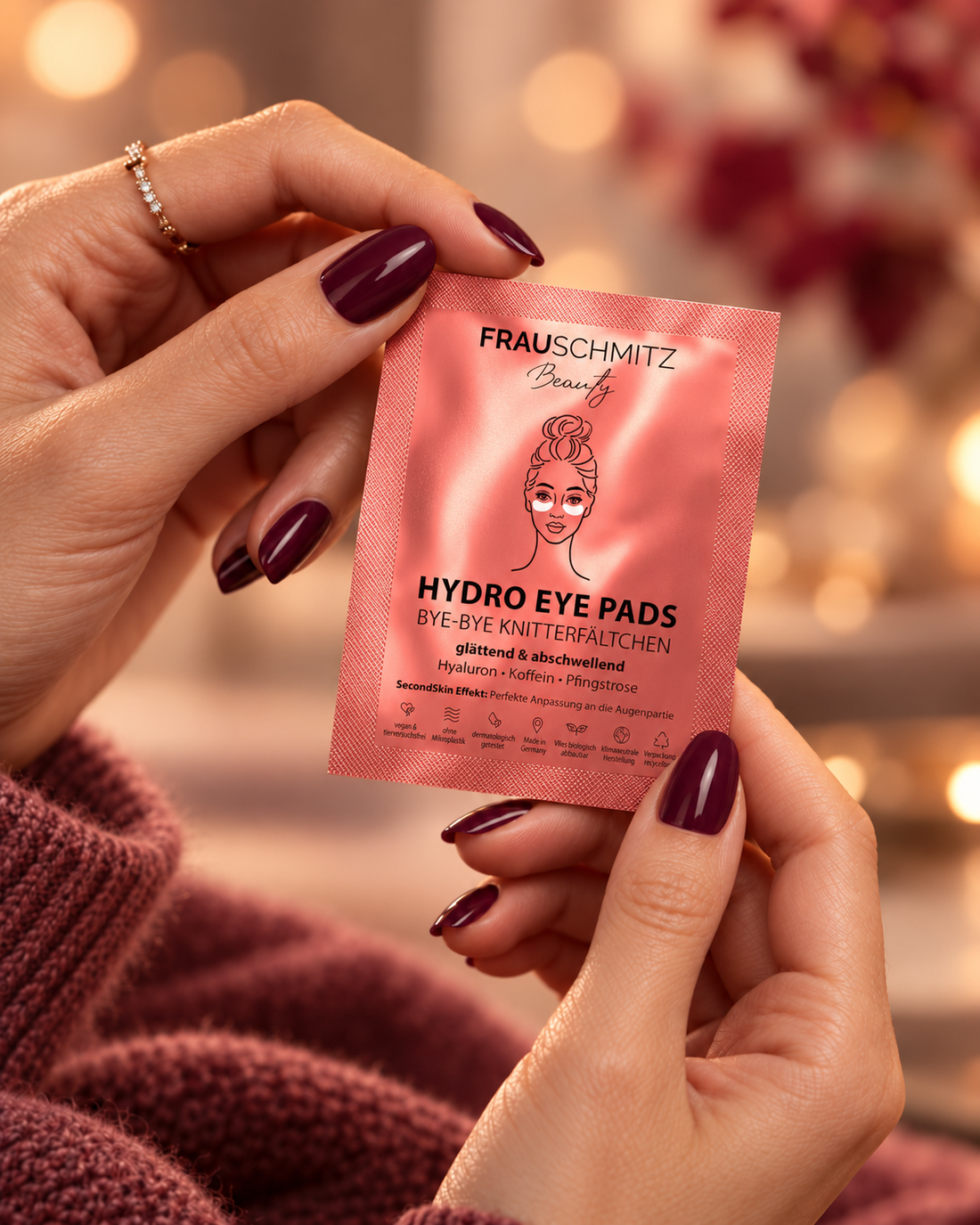 Gepflegte Hände im Strickpullover halten ein FRAUSCHMITZ Hydro Eye Pads Sachet im warmen Herbstlicht